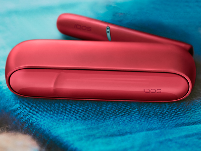 IQOS Originals Duo holder with HEETS stick and pocket charger in red color, on a coffee table.