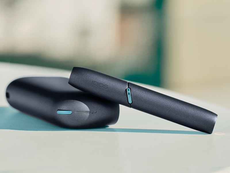 IQOS Originals Duo Holder and Pocket Charger in black color on a coffee table.