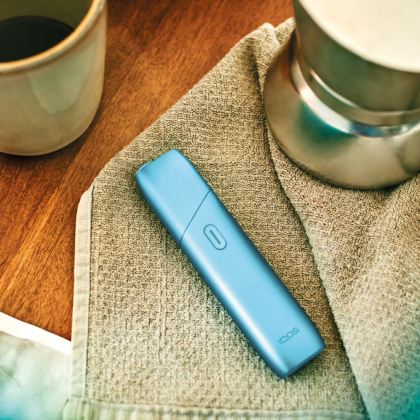 Turquoise IQOS Originals One heated tobacco device on a coffee table.