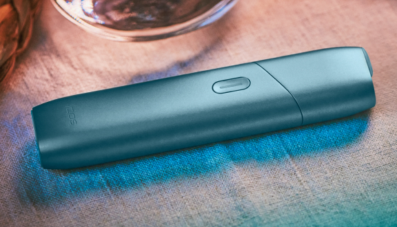 Turquoise IQOS Originals One heated tobacco device on a fabric table mat.