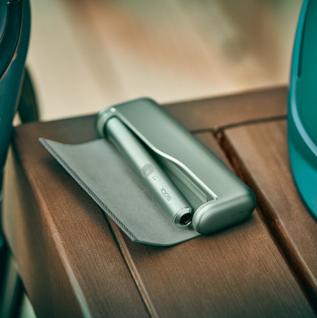 Moss Green IQOS ILUMA držalo in žepni polnilnik na mizi.