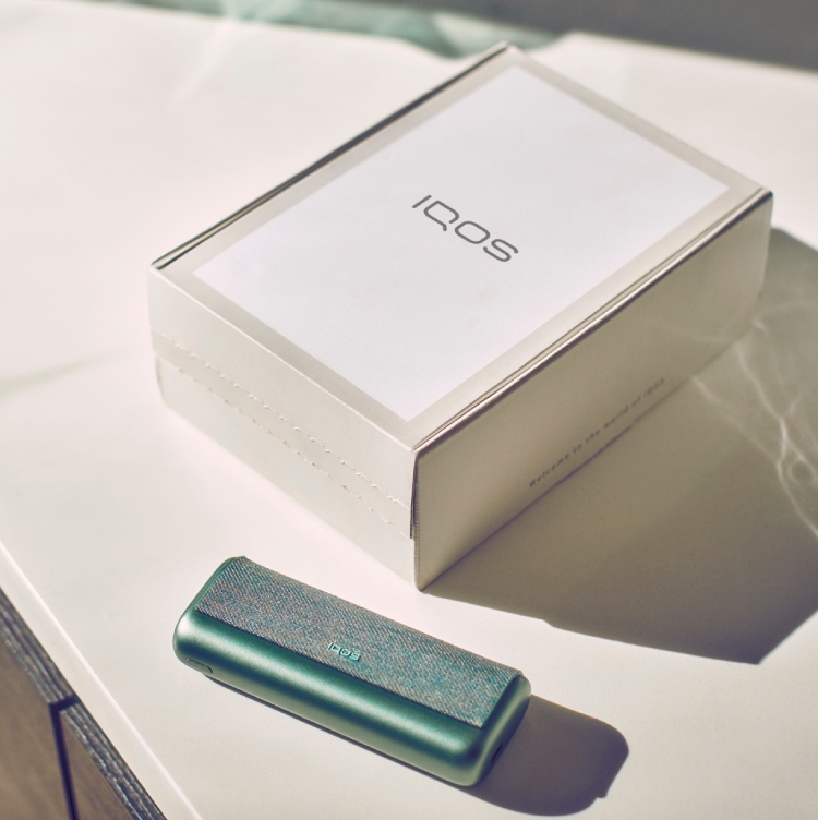 Jade Green IQOS ILUMA PRIME žepni polnilnik in IQOS škatla na mizi.